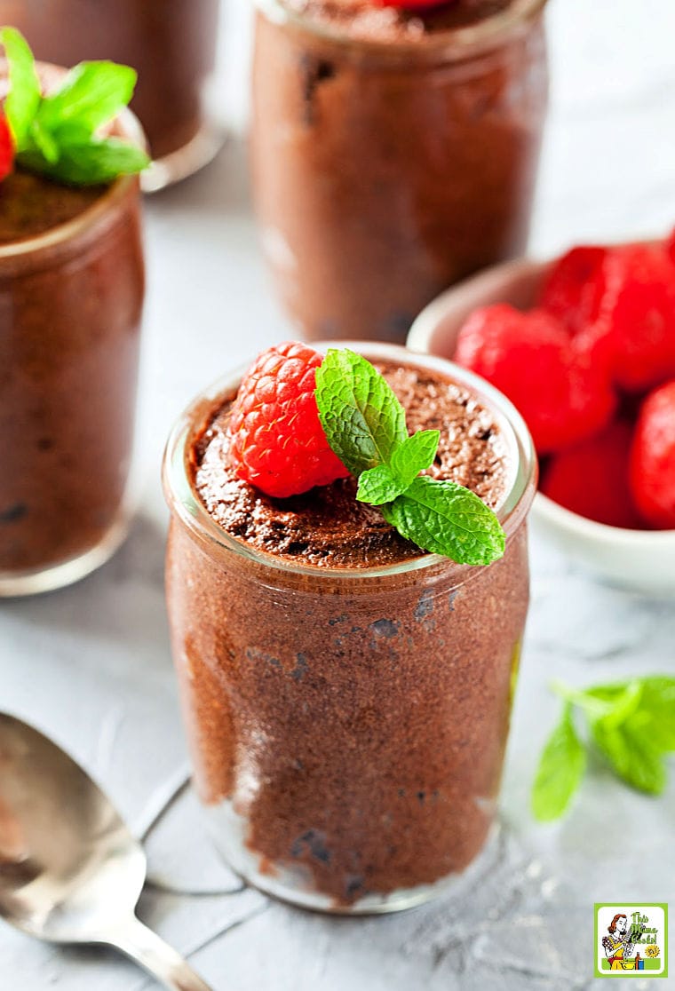 Glasses of chocolate mousse served with garnish of raspberries and mint with a silver spoon.
