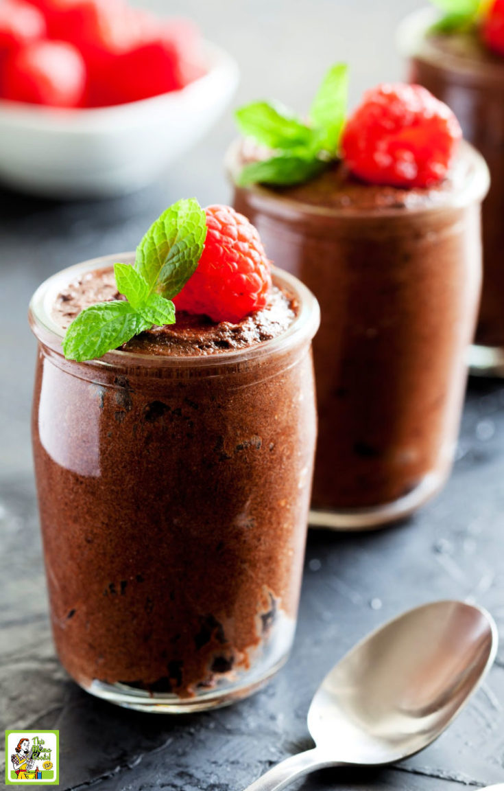 Glasses of chocolate mousse garnished with raspberries and mint. Spoon and bowl of raspberries.