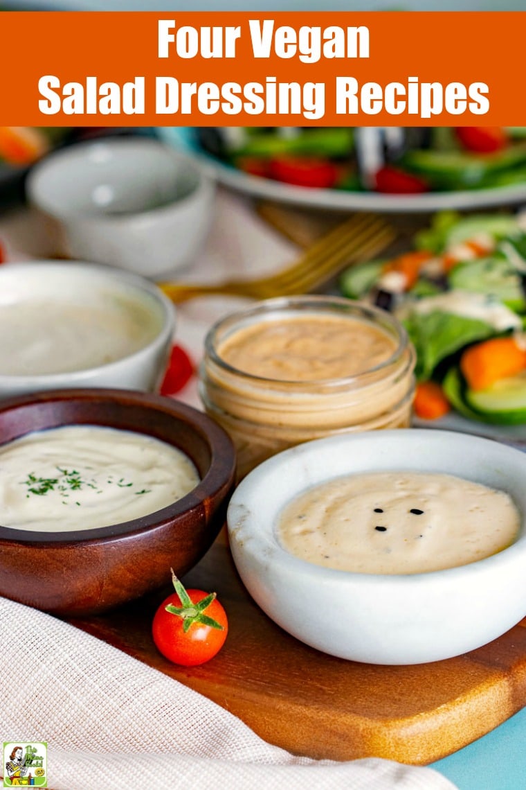 Bowls and jars of vegan salad dressing with plates of salads on a wooden cutting board with napkins and forks.