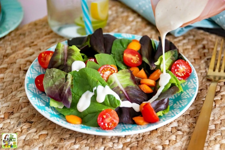 Creamy Italian poured on salad with tomatoes on a blue plate with a fork on a woven mat.