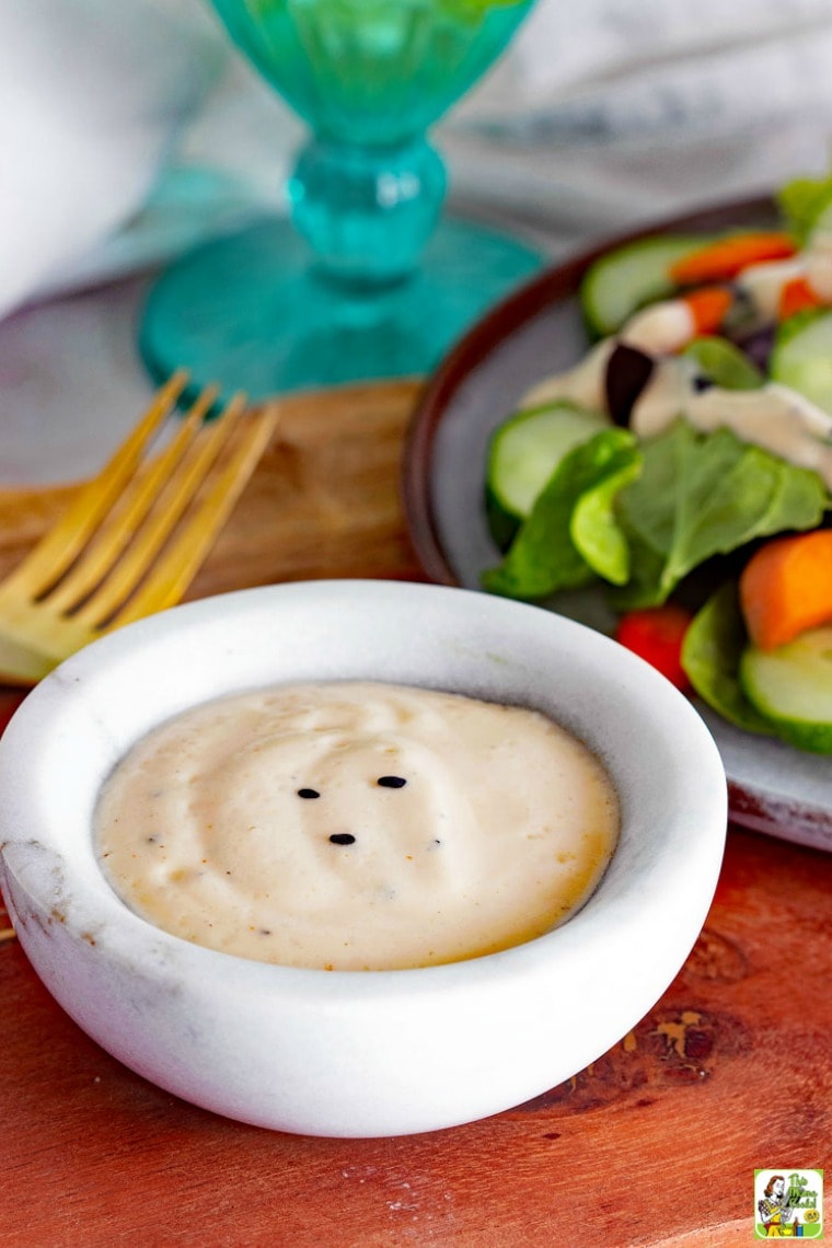 A small bowl of Spicy Sesame Ginger Vegan Salad Dressing with salad and a gold fork on a wooden cutting board.