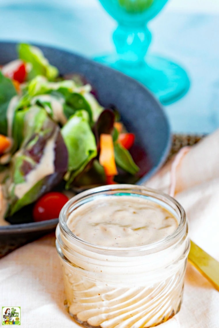 Sundried Tomato & Balsamic Vegan Dressing in a jar with a plate of dressed salad with fork and napkin.