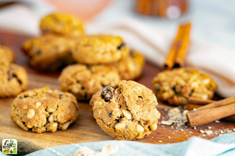 A pile of Pine Nut Cookies on a wooden cutting board with cinnamon sticks with blue cloth napkins.