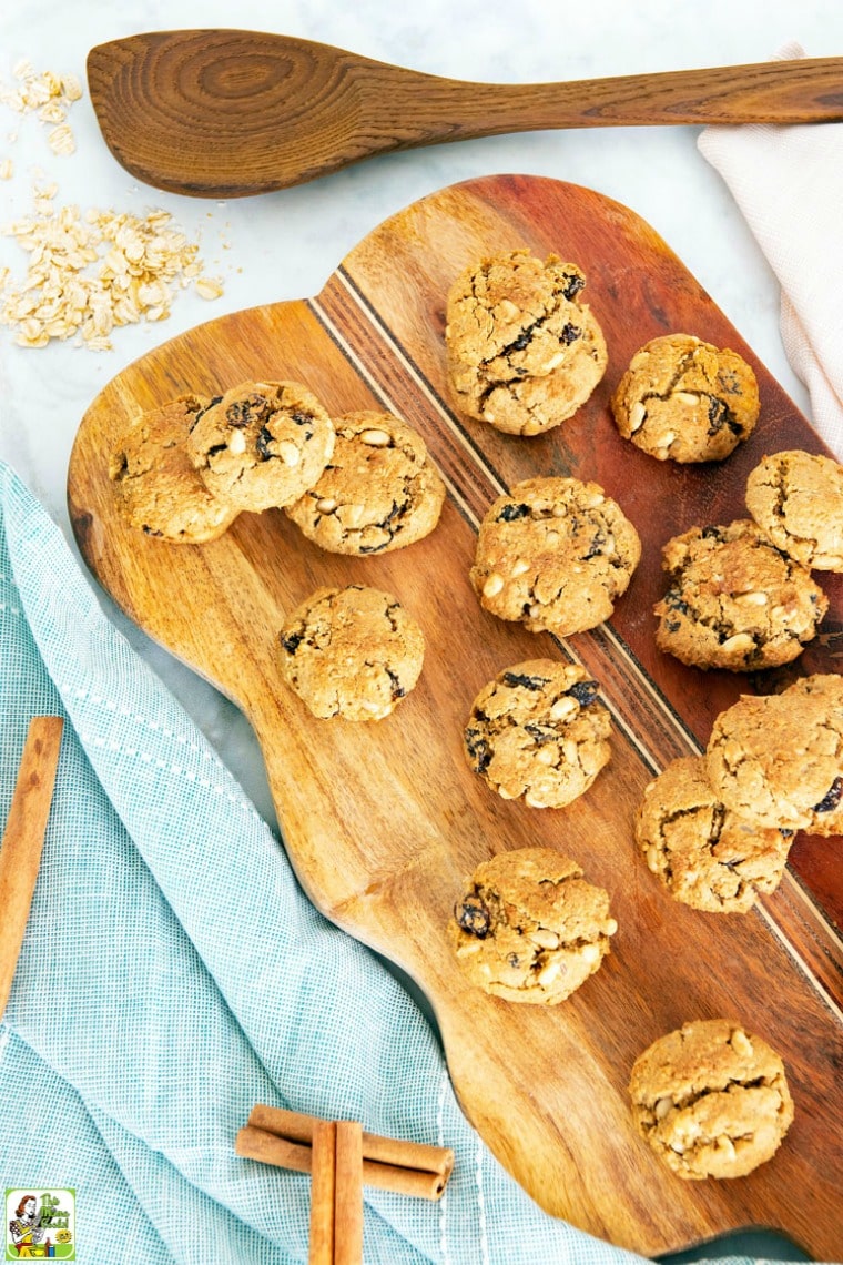 A pile of Pine Nut Cookies on a wooden cutting board with cinnamon sticks with blue cloth napkins.