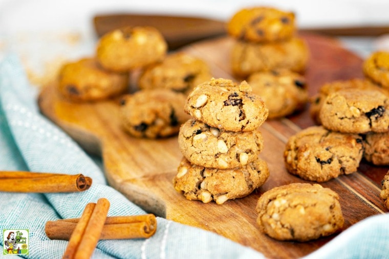 Stacks of pine nut and raisin cookies on a wooden cutting board with cinnamon sticks.