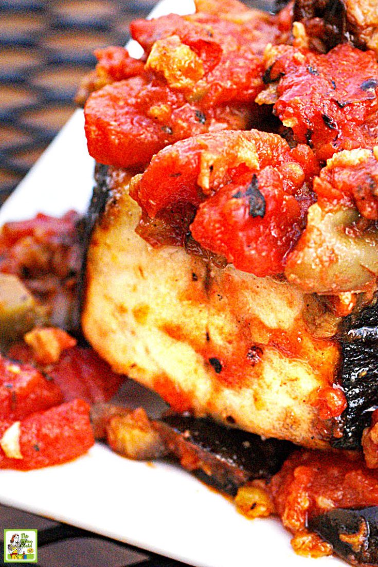 Closeup of a grilled wahoo steak with cooked tomatoes and olives on a white plate.