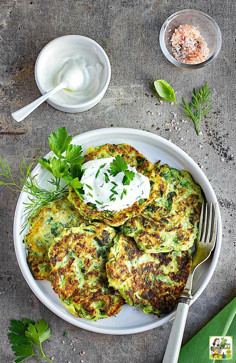 Overhead shot of A plate of Zucchini Fritters with bowl of sour cream and some salt.