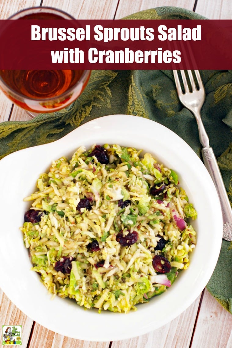 A bowl of brussel sprouts salad with cranberries with a glass of tea and a fork.