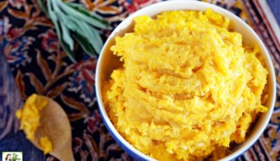 A bowl of mashed sweet potatoes with parsnips with a wooden spoon and sprig of sage.