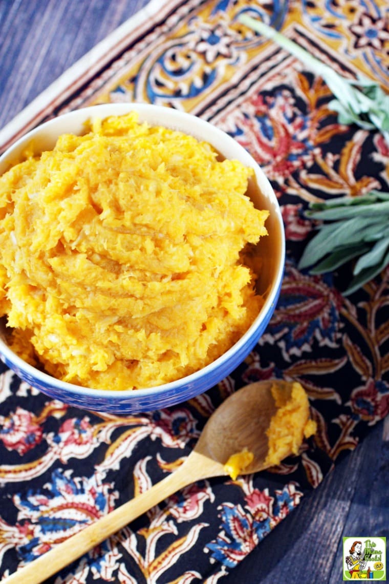 A sprig of sage, a wooden spoon, and a blue bowl of Mashed Sweet Potatoes with parsnips.