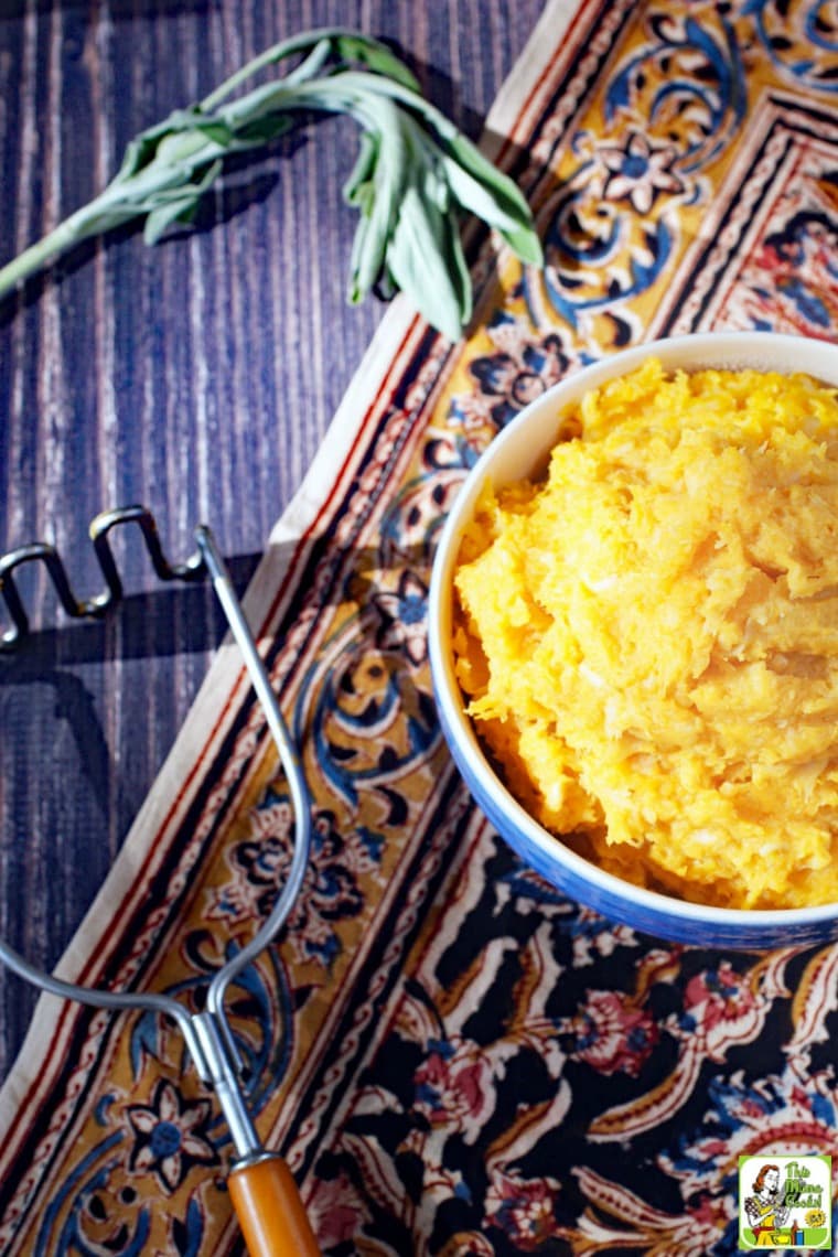 An antique potato masher and a bowl of mashed sweet potatoes on a patterned napkin.