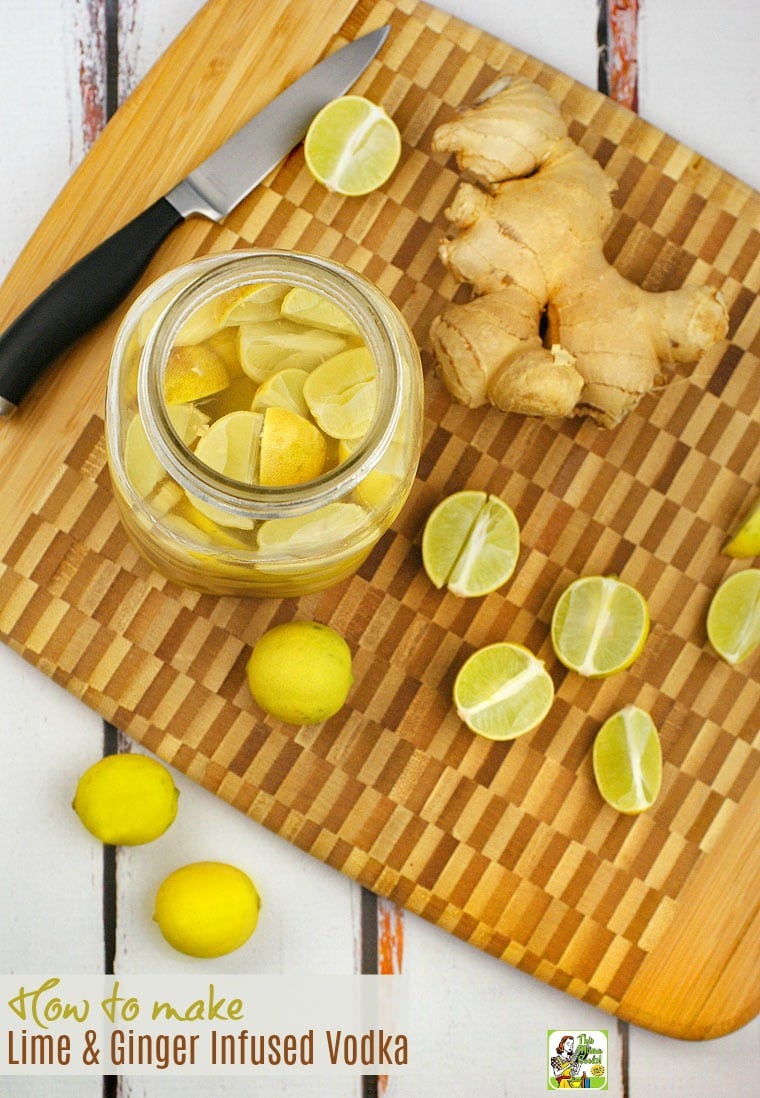 A mason jar of Lime & Ginger Infused Vodka on a wooden cutting board with limes and ginger and a knife.