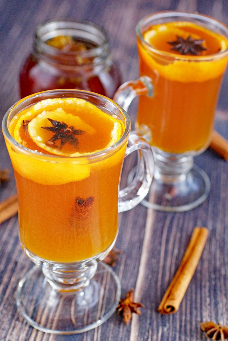 Glass mugs of hot toddy with tea and orange peels, star anise and cloves with a jar of honey.