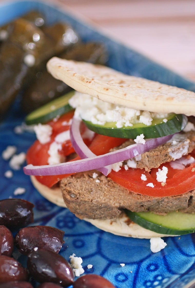 Closeup of a homemade gyro sandwich on a blue plate with olives and stuffed grape leaves.