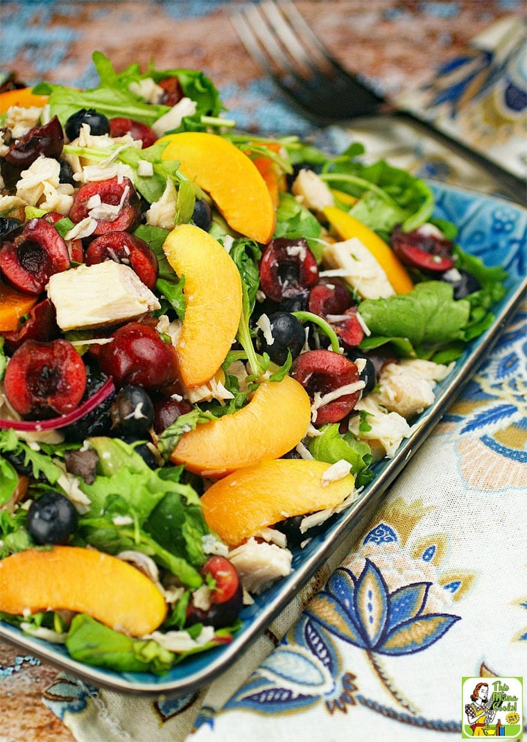 Mixed green salad with chicken, peaches, cherries, and berries on a blue plate.