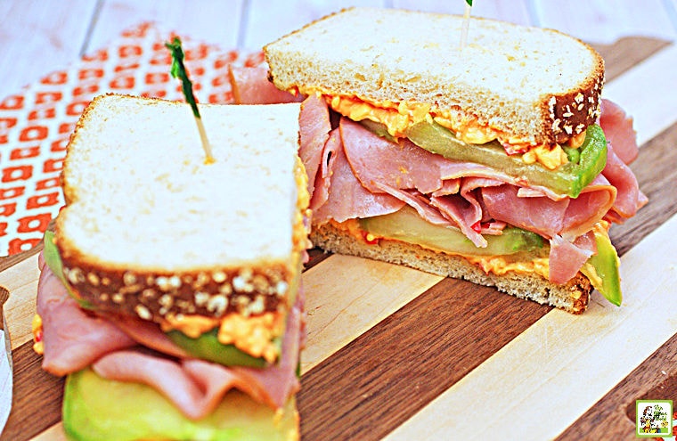 Ham & Pimento Cheese Sandwich cut in half on a wooden cutting board with an orange and white napkin.