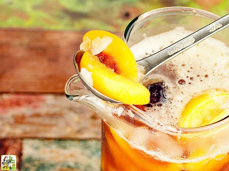 A slice of peach in a serving spoon above a pitcher of iced tea sangria.