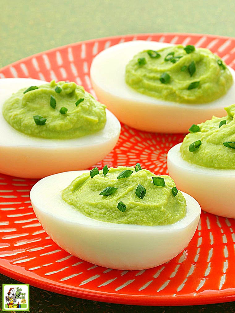 An orange plate filled with Avocado Deviled Eggs with chives.