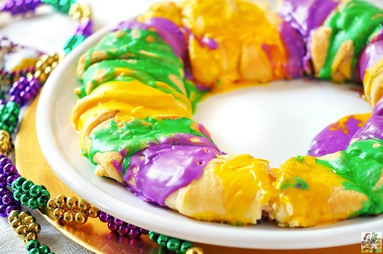 King Cakes with Cream Cheese Cinnamon Filling on white and gold plates with purple, green, and gold Mardi Gras beads.