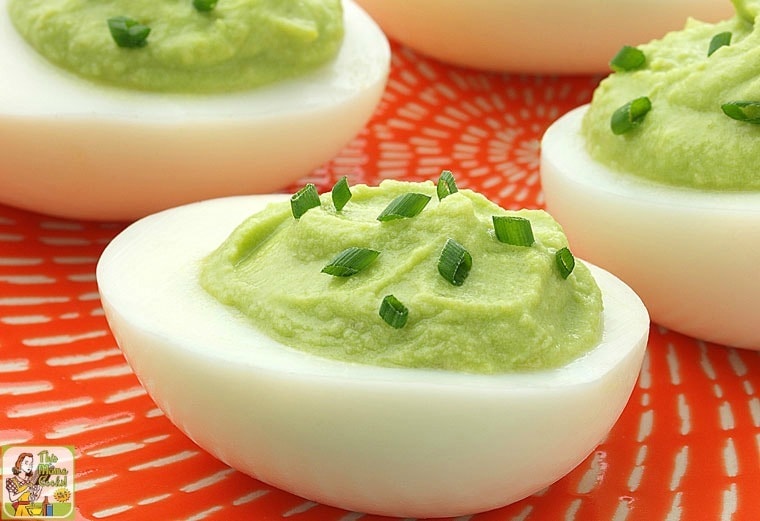 Closeup of avocado deviled eggs on an orange plate.