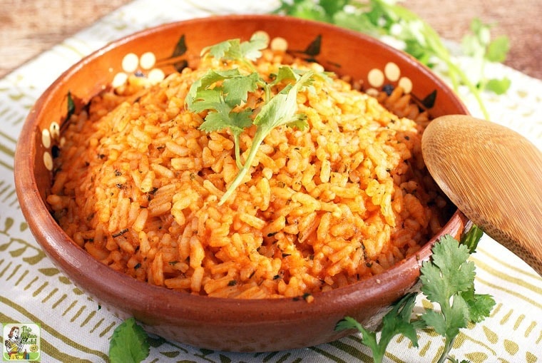 Mexican rice in a ceramic bowl with a wooden spoon on a cloth napkin with sprigs of cilantro.