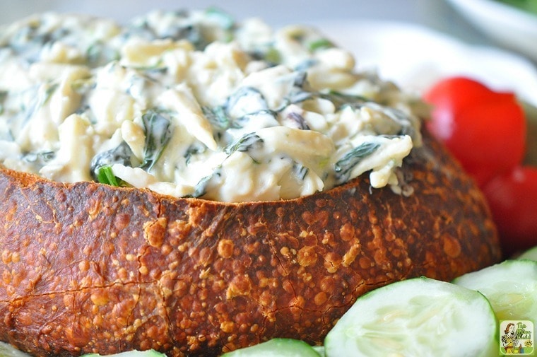 Hot Crab Spinach Dip in Baked French Dip Bread Bowl with cucumber slices and cherry tomatoes.