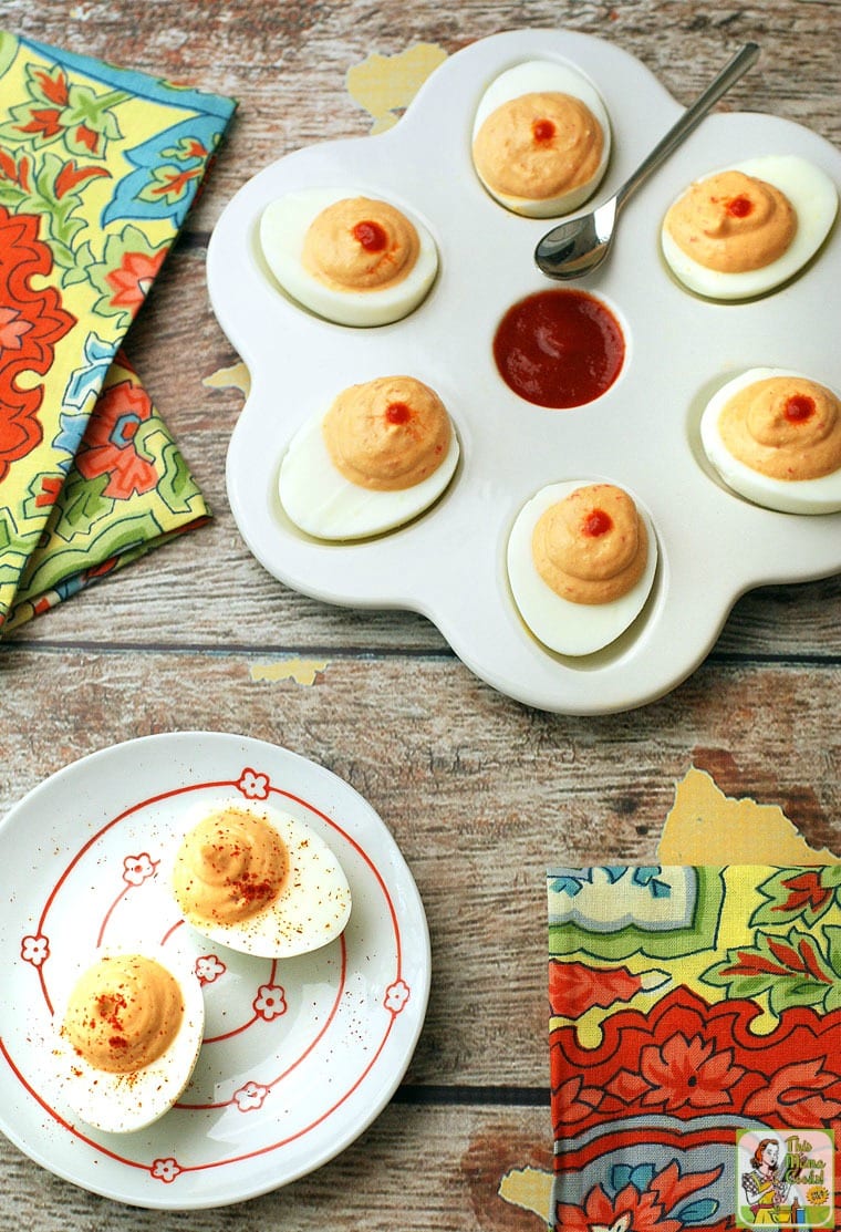 Two plates of Sriracha Deviled Eggs with napkins and serving spoon.