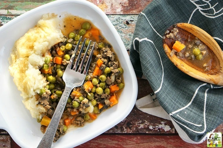 A plate of Shepherd's Pie with Ground Turkey Recipe with a platter of shepherd's pie and a wooden spoon in the background