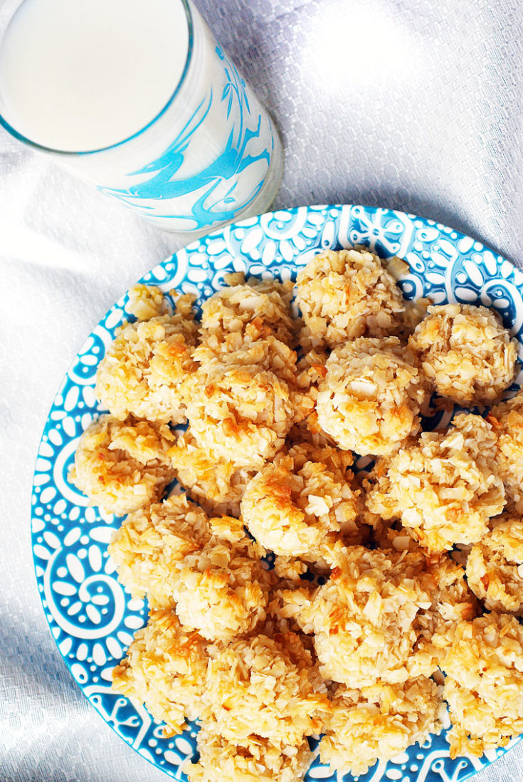 A blue and white plate of coconut macaroons and a glass of milk on a white tablecloth.