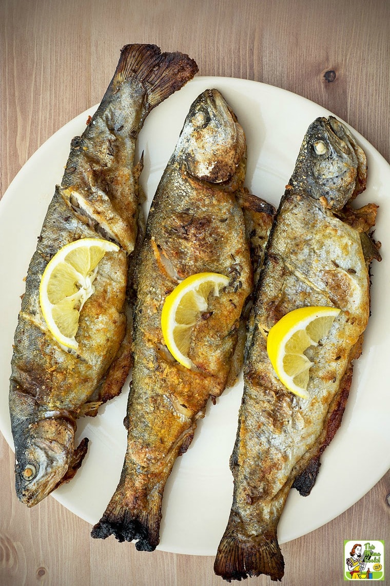 Three smoked trout fish on a white plate covered in lemon slices.