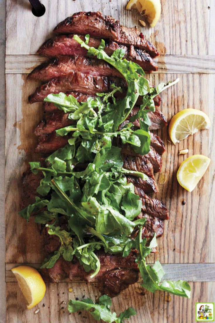 Sliced grillied flank steak with arugula on a wooden with lemon slices.