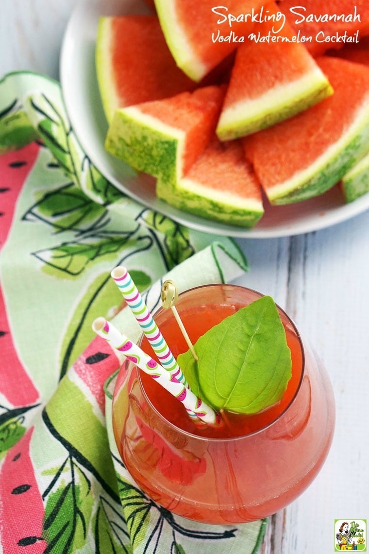 A glass of Vodka Watermelon Cocktails with a colorful paper straw, a pink and green napkin, and a plate of watermelon.