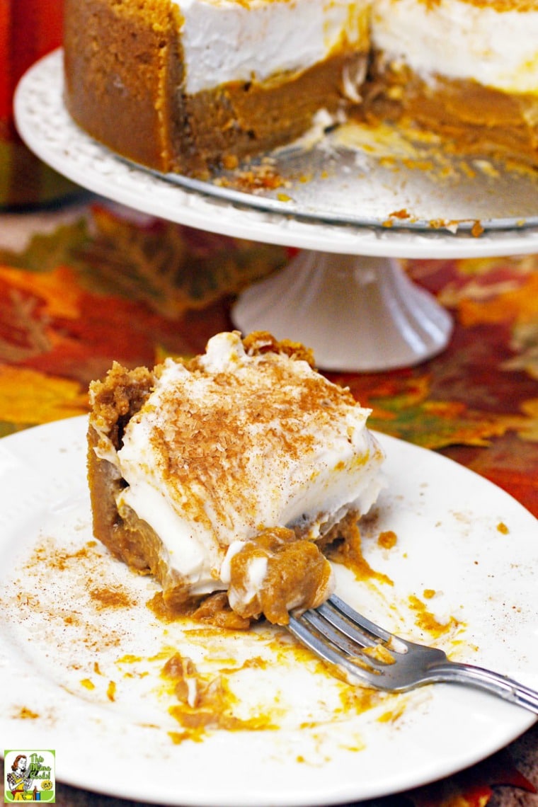 A slice of creamy pumpkin pie with fork and a cake stand in the background.