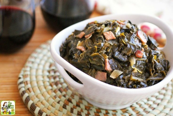 A white bowl of easy sweet collard greens on a woven mat with red wine glasses in the background.