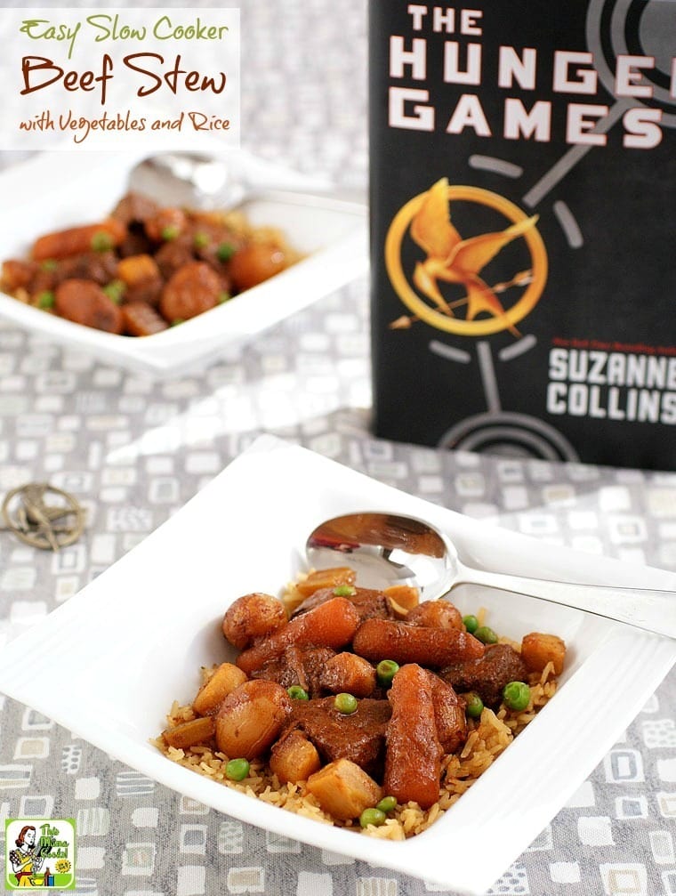 White bowls of Slow Cooker Beef Stew with peas, carrots and potatoes with spoons shown with The Hunger Games book and pin.