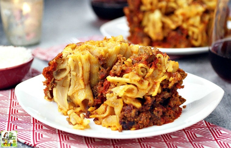 A plate of slow cooker baked ziti on a napkin with a wine glass and bowl of grated cheese.
