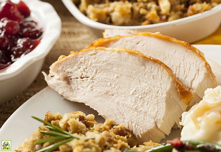 Slices of smoked and rubbed turkey on a platter with stuffing with side dishes in the background.