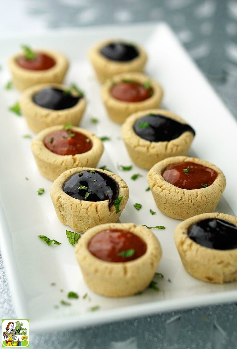 A long rectangular white plate of purple and orange Fruit Filled Cookie Cups with mint garnish on a silver background.
