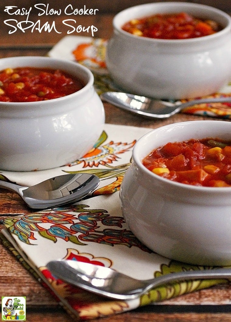 Closeup of white ceramic bowls of SPAM and vegetable soup, spoons, and colorful floral napkins on a wooden countertop.