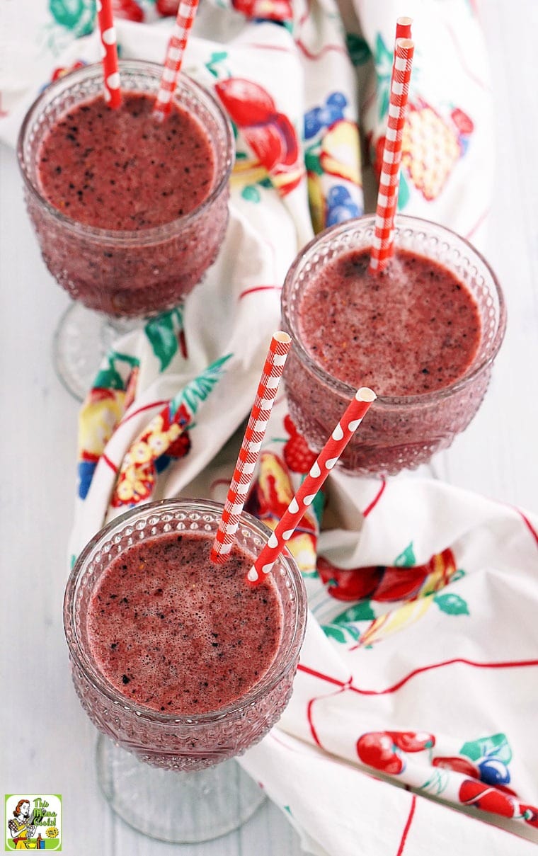 Overhead view of three glasses a berry smoothie with red straws on a vintage tablecloth.