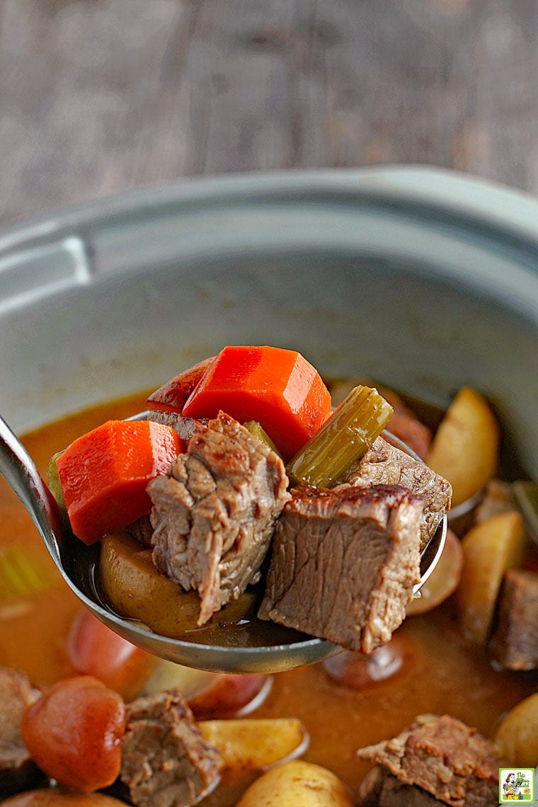 Closeup of a spoonful of venison and vegetable stew above a crockpot of stew.