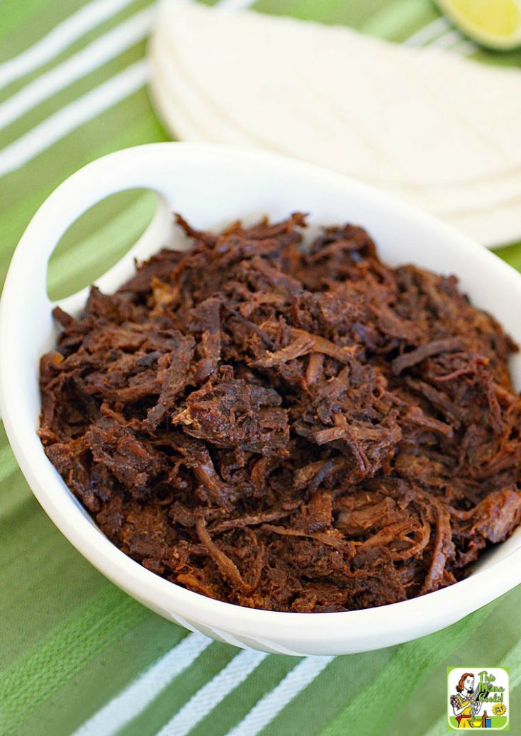 A bowl of shredded Slow Cooker Goat with tortillas in the background.