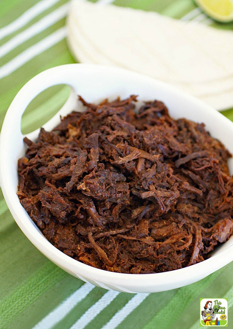 A bowl of shredded slow cooker goat with tortillas in the background.