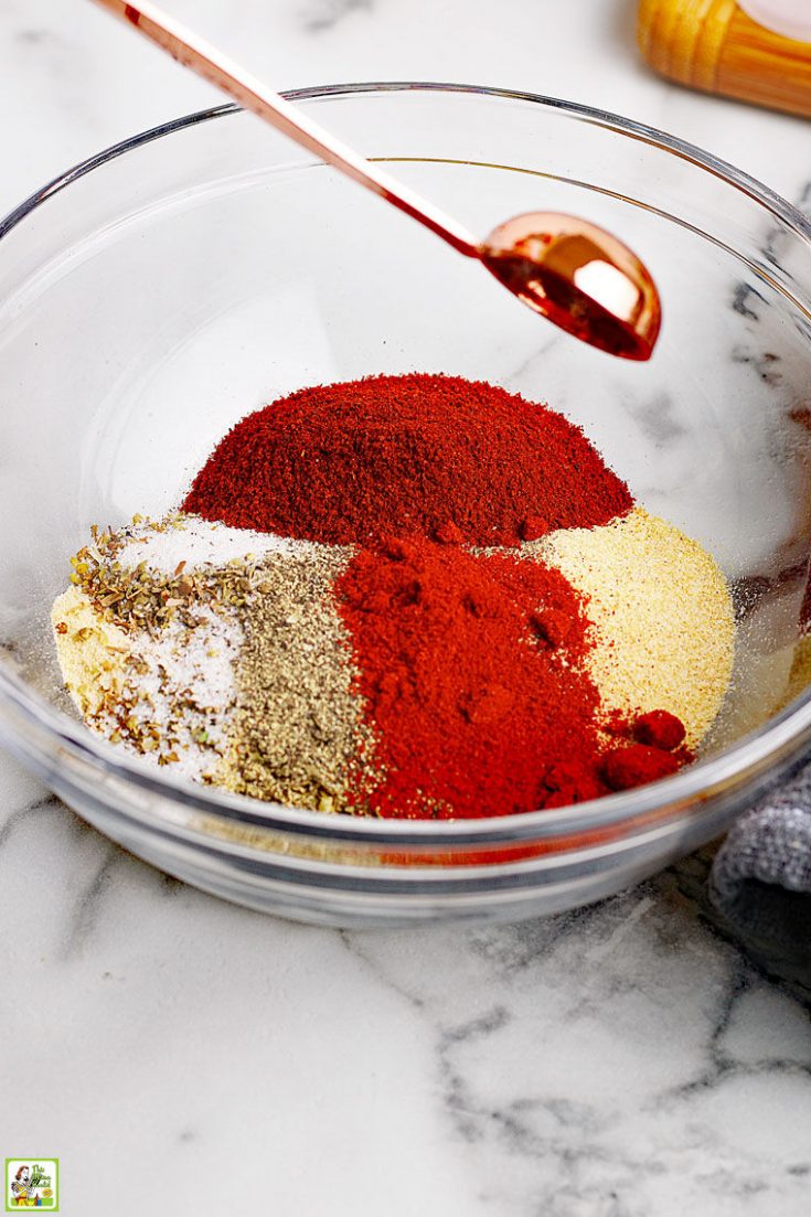 Making homemade taco seasoning in a glass bowl with a variety of seasonings and a copper measuring spoon.