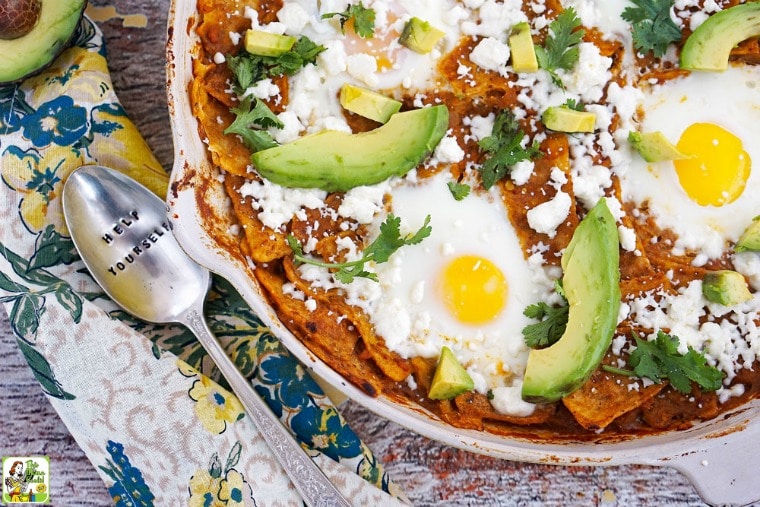 Breakfast chilaquiles in a skillet with eggs, avocados, and cilantro with a cloth napkin and serving spoon.