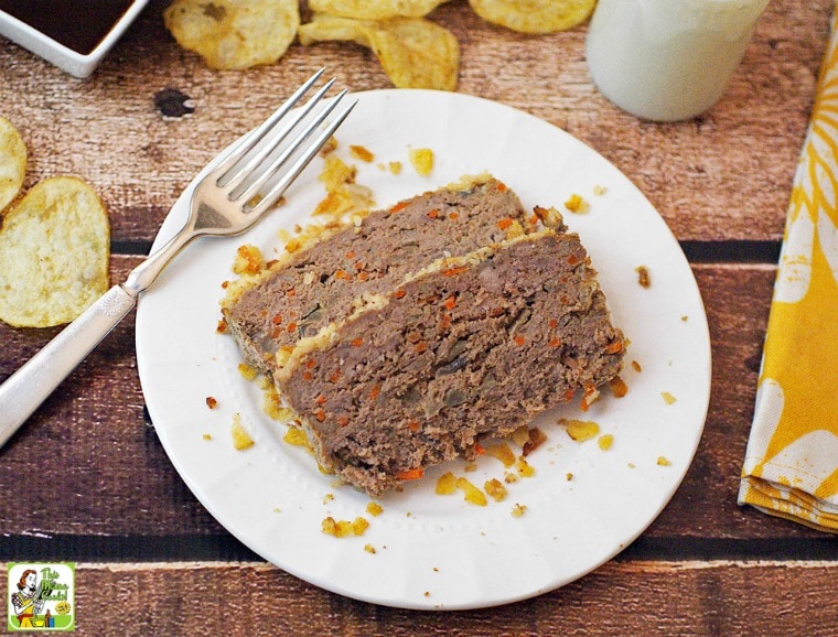 A plate of Gluten Free Meatloaf with Potato Chips & Carrots, fork, glass of milk, yellow napkin, potato chips, and dish of BBQ sauce.