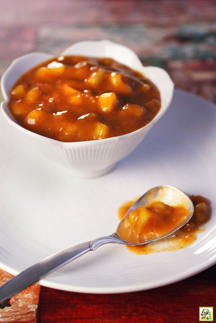 A bowl of healhty apple pie filling with a spoon on a large white plate.