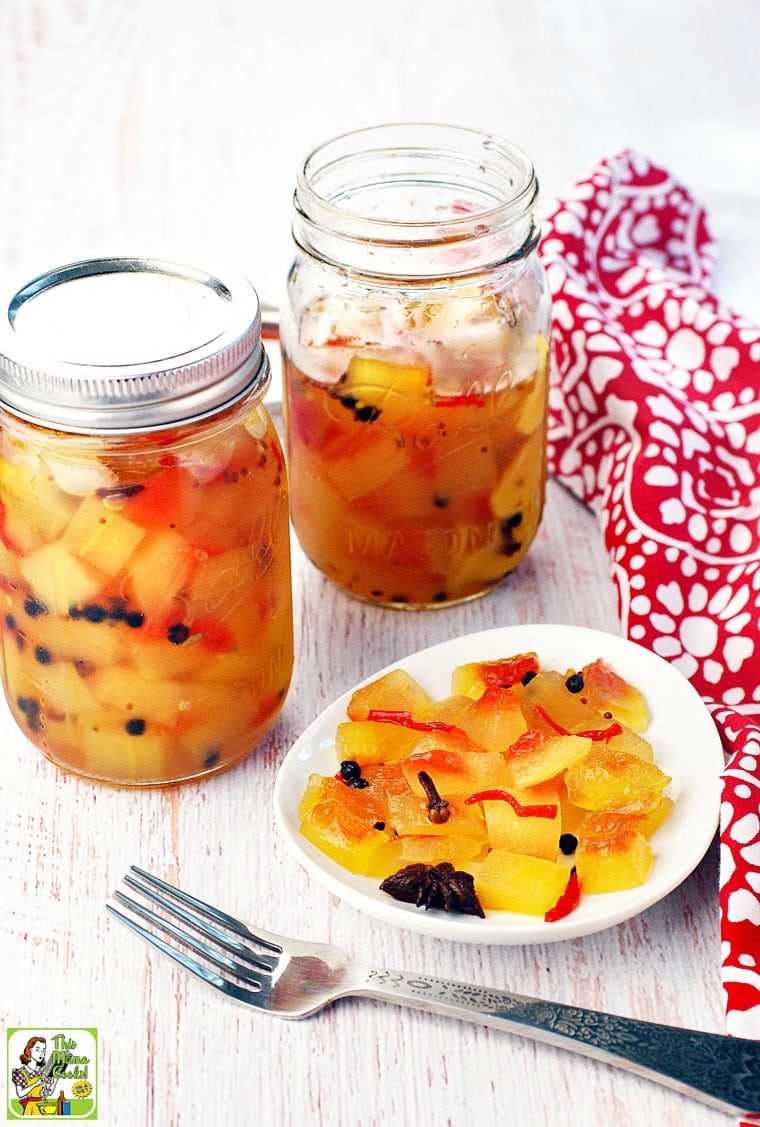 Two Mason jars and a white plate of crisp watermelon rind pickles with fork and red and white napkin.