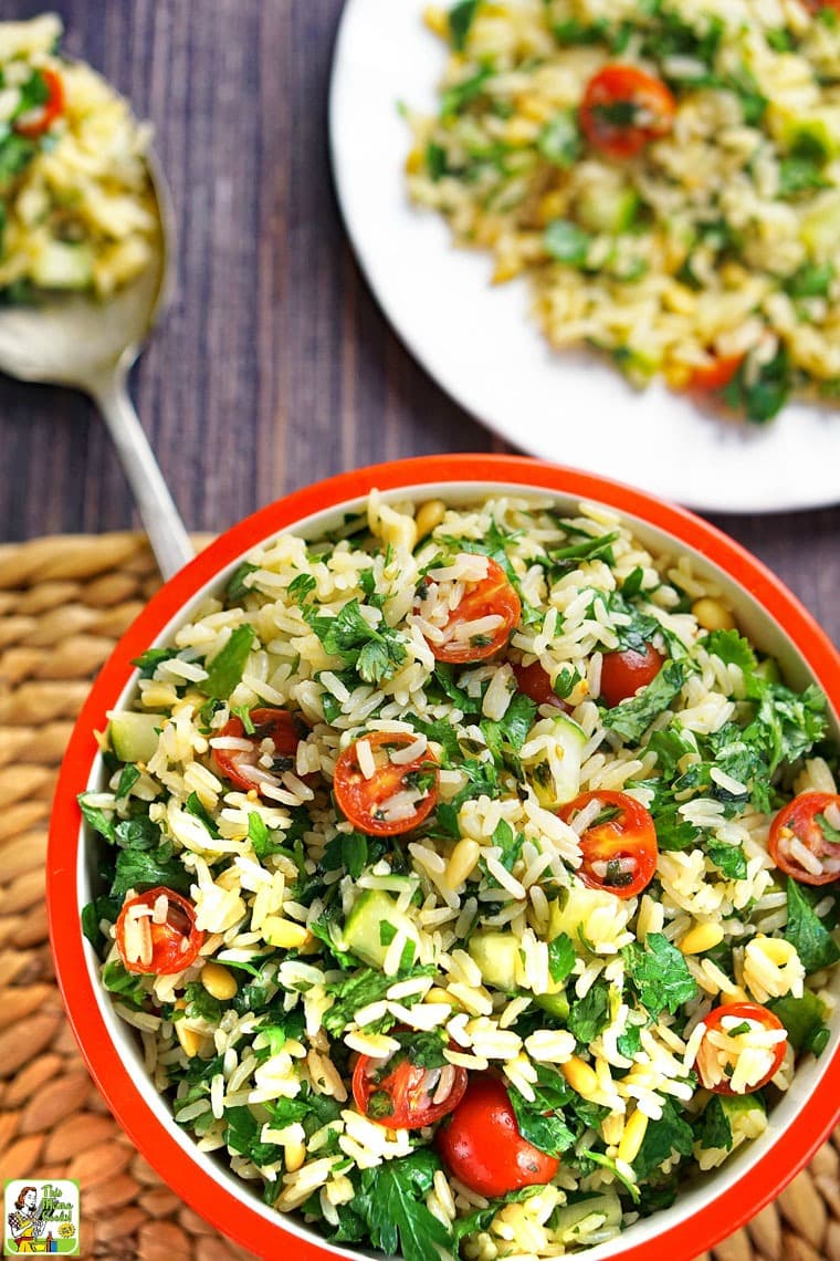 Closeup of a bowl of tabbouleh rice with tomatoes and parsley with plate and serving spoon in the background.