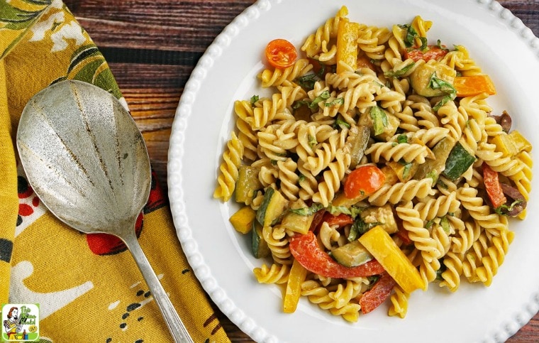 Pasta Salad with Roasted Vegetables on a white plate with serving spoon and napkin.